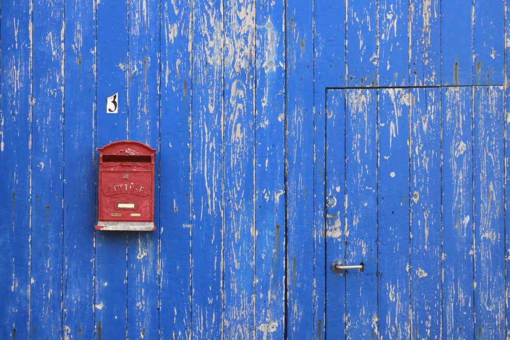 Distressed, blue barn with a door and a red mailbox.