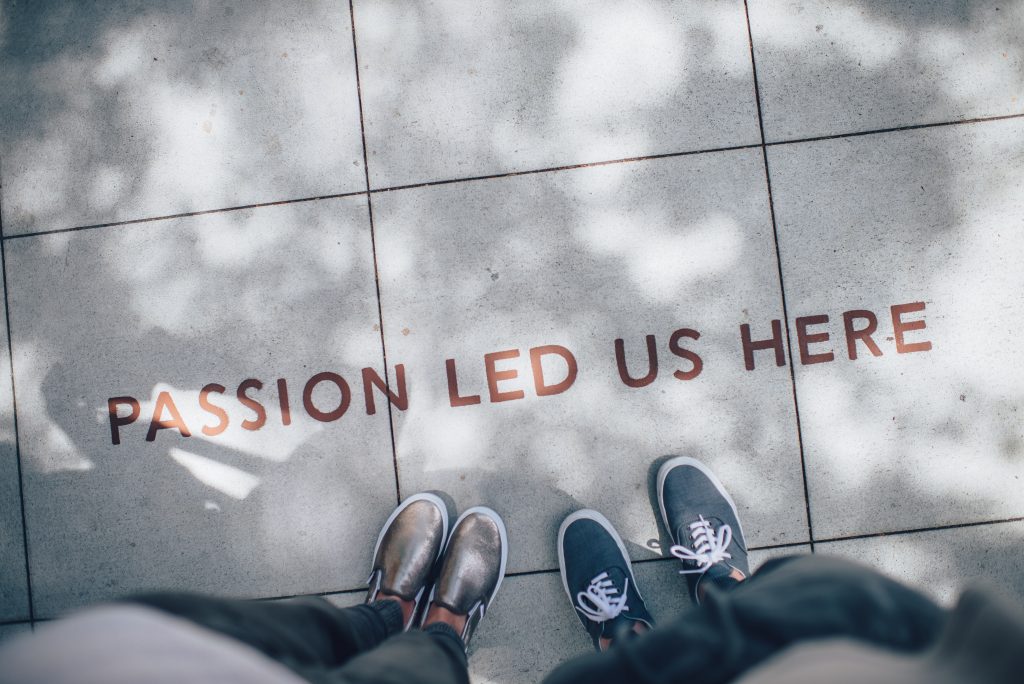 Two people looking down at a sidewalk with 'passion led us here' engraved on it.