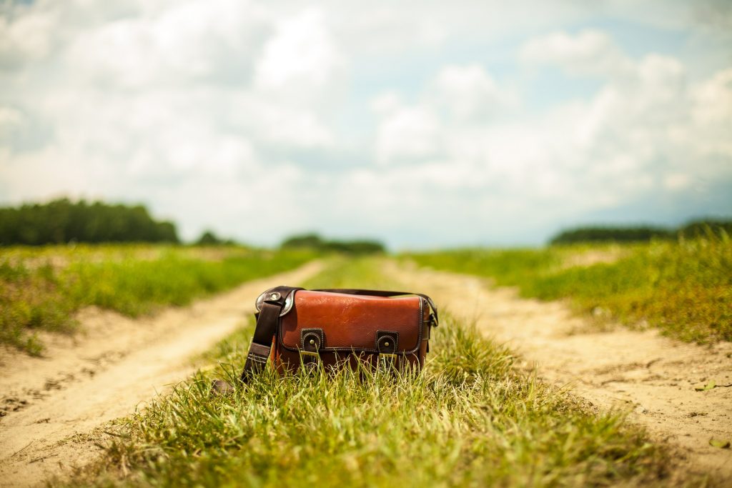 Leather messenger bag sitting in the middle of a dirt road looking toward the horizon.