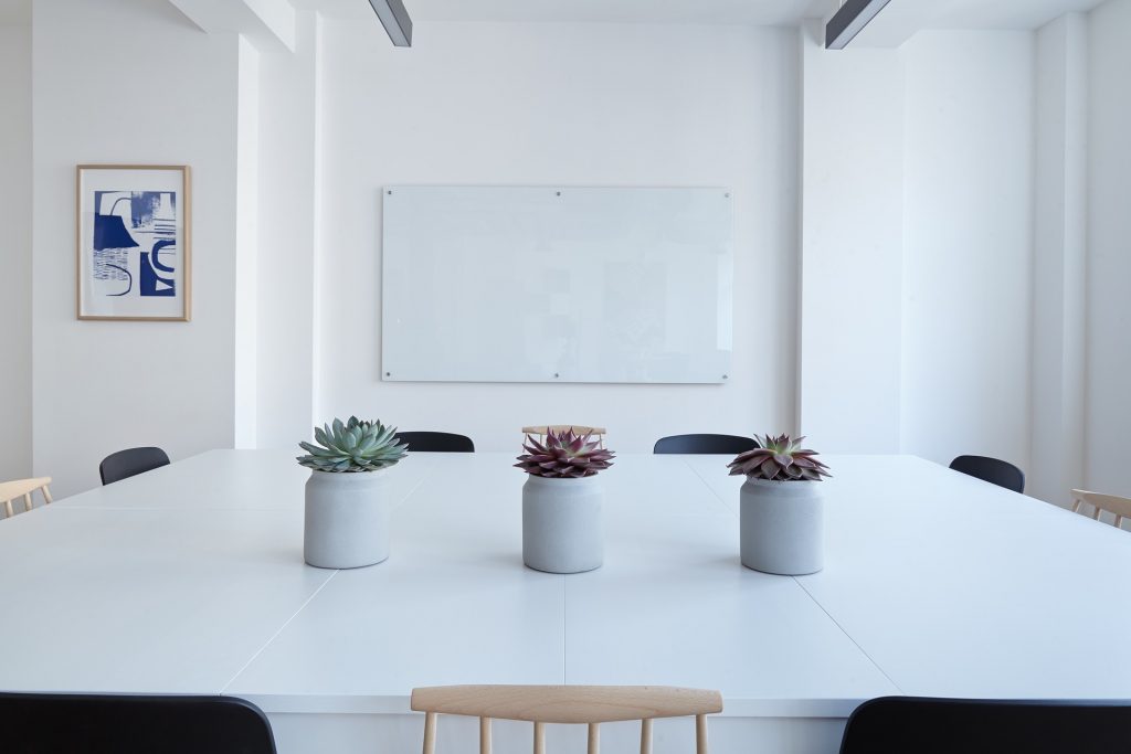 Three chairs behind a glossy white table facing a whiteboard. Ready for a workshop.