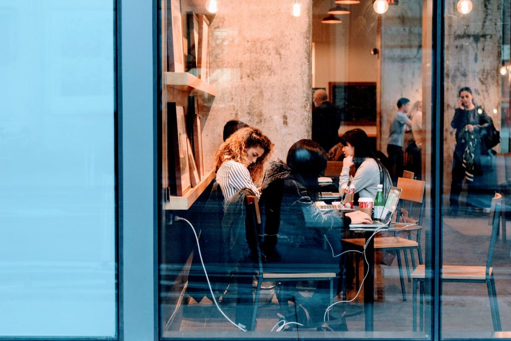 College students working on laptops at a table in a cafe.