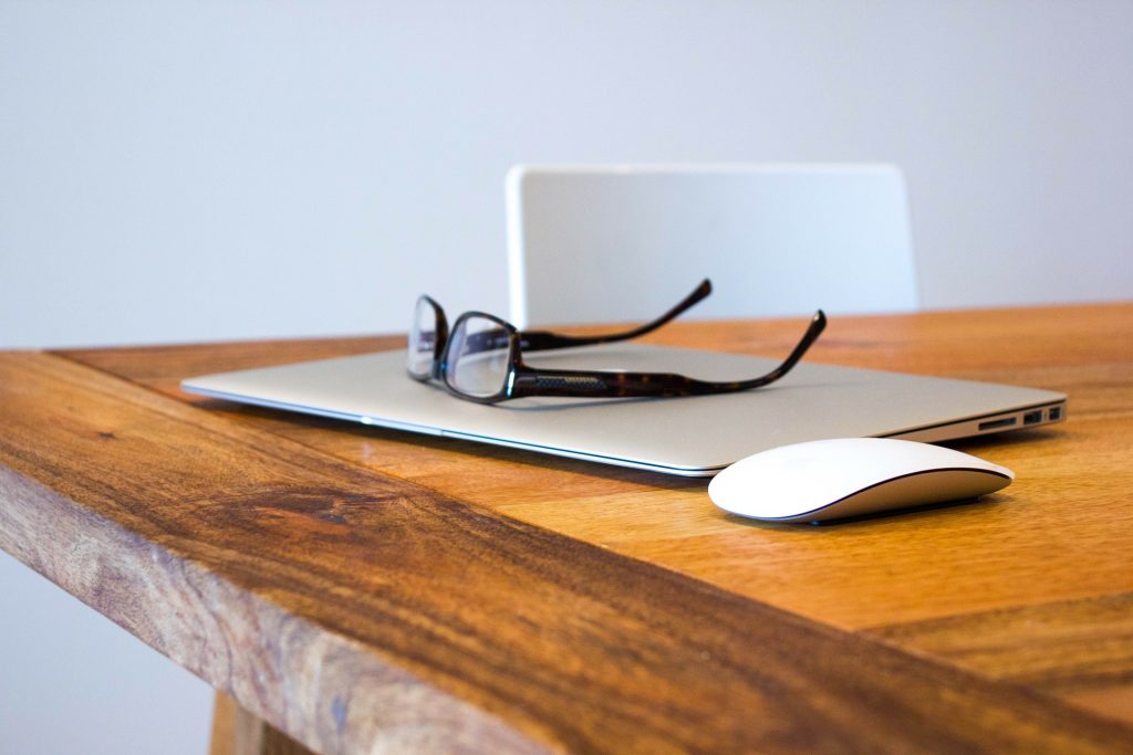 Laptop, glasses, computer mouse sitting on a wooden table