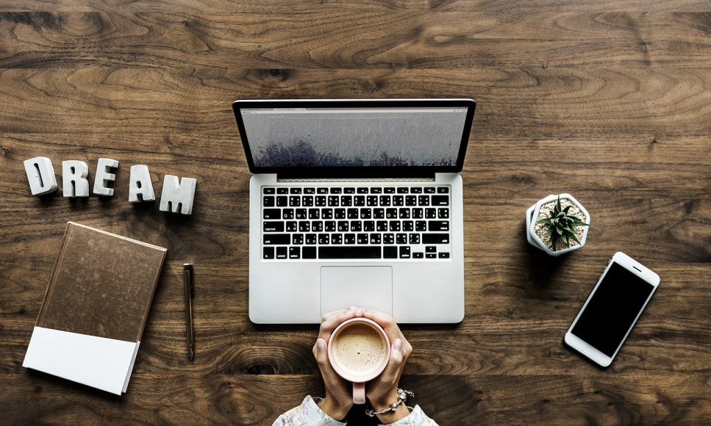 Woman sitting in front of a laptop holding a coffee cup.