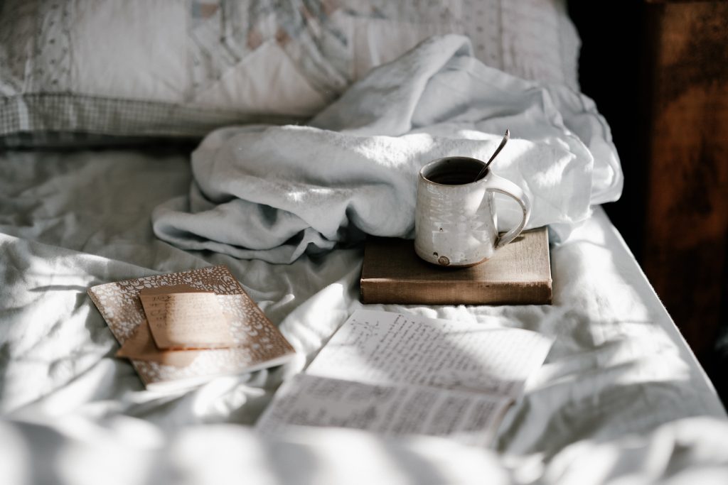 Cozy blanket on a bed with a few notebooks and a cup of tea.