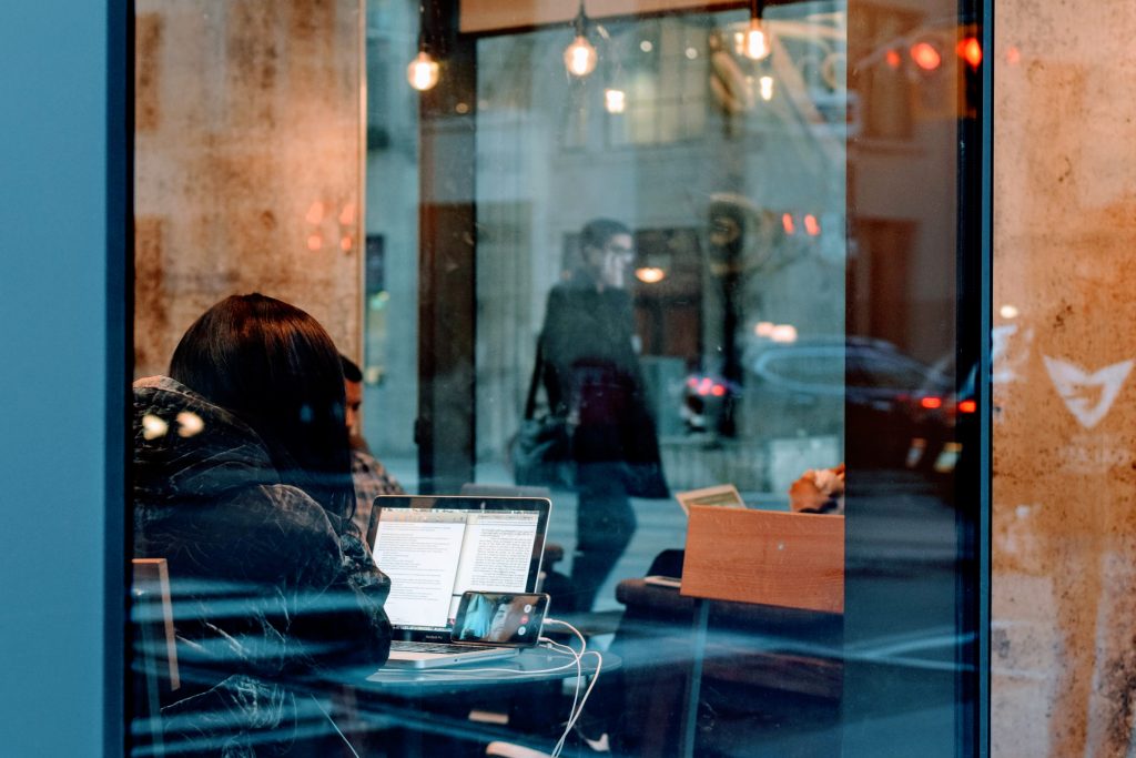 Looking through cafe window at a college student working on a laptop.